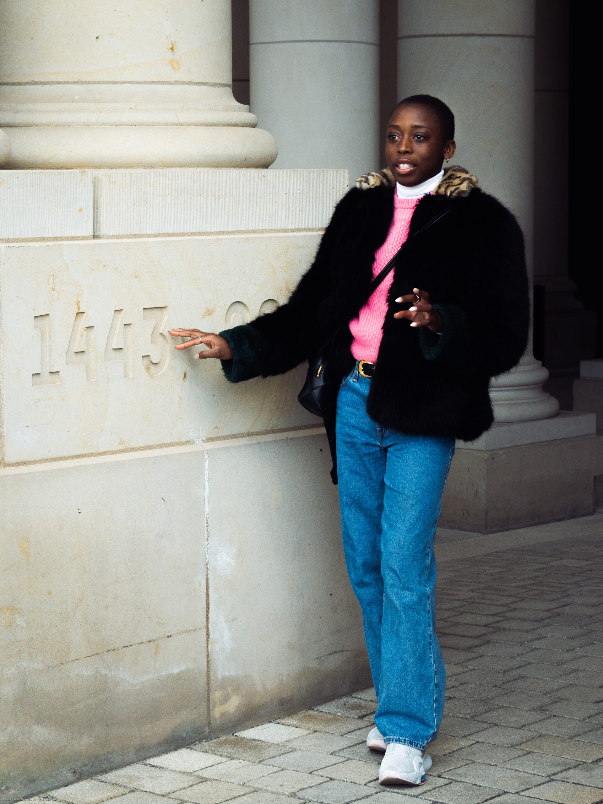 Berliner_Schloss_Hohenzollern - Dekoloniale Stadtführung Person in schwarzem Pelzmantel und pinkem Pullover steht neben einer Säule mit der Jahreszahl 1443. Hintergrund des Berli...