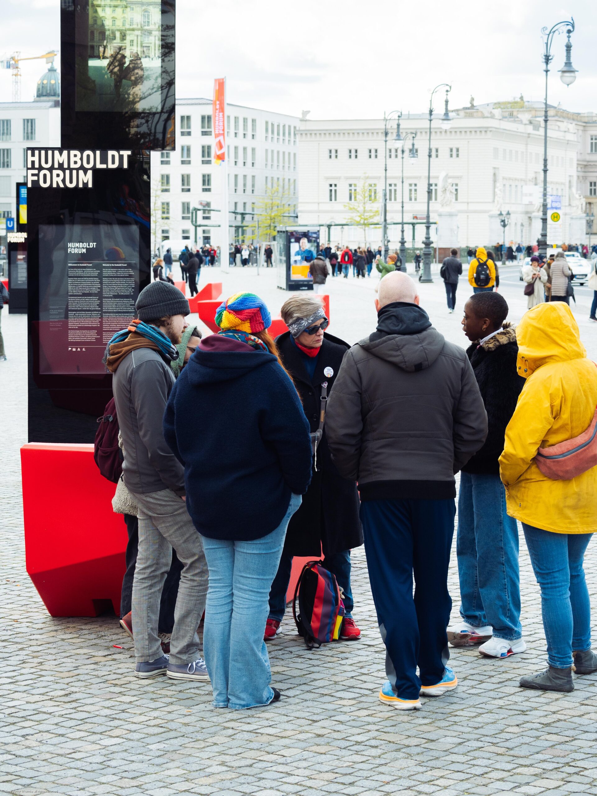 schlossplatz - Dekoloniale Stadtführung Gruppe von Menschen, die sich am Schlossplatz um einen Informationsstand des Humboldt Forums versammelt haben.
