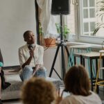 Sprecherin mit Mikrofon sitzt auf einer Couch während einer Diskussion über Antirassismusarbeit in einem hellen Raum.