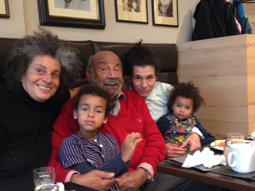 Family with two children and two adults sitting in a café and smiling. Background with pictures on the wall.